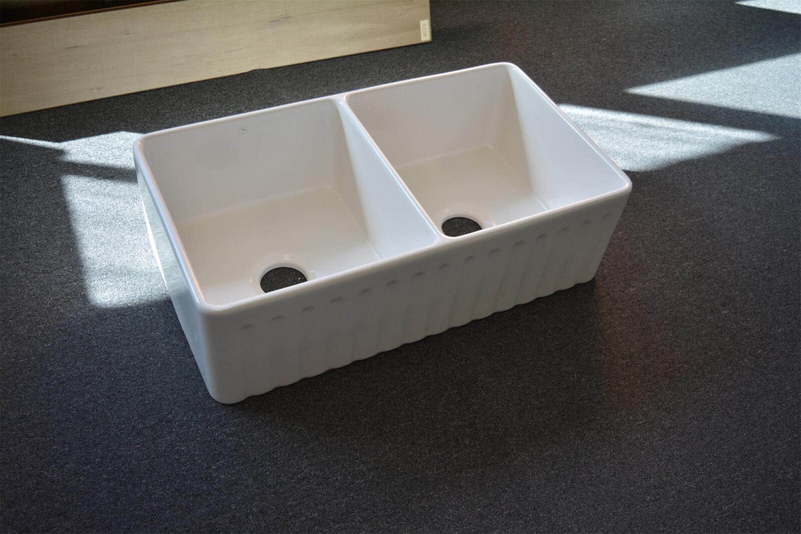 Double bowl white kitchen sink on dark carpet.