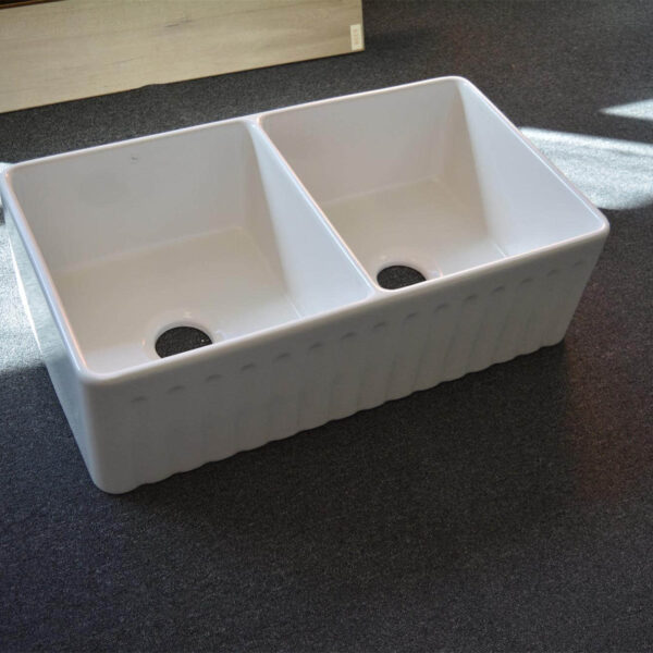 Double bowl white kitchen sink on dark carpet.