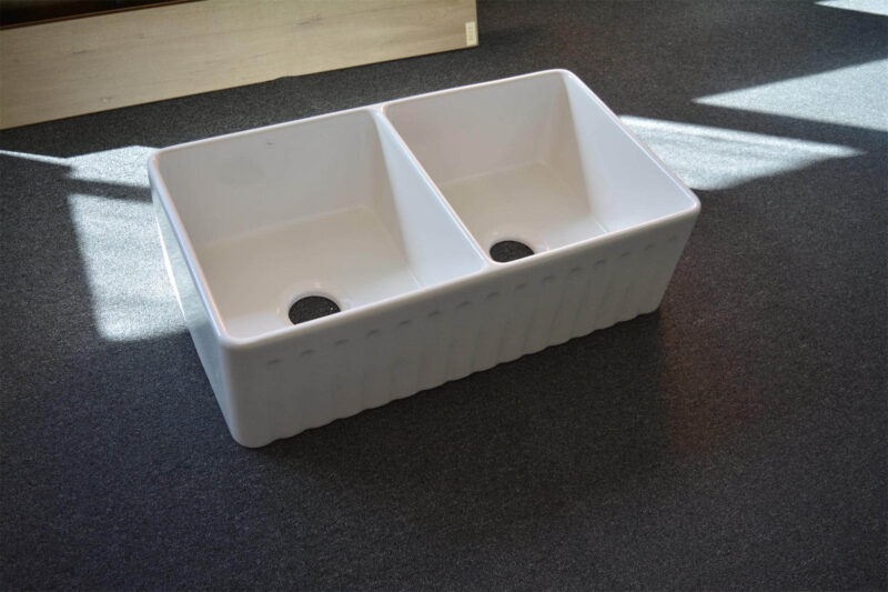 Double bowl white kitchen sink on dark carpet.