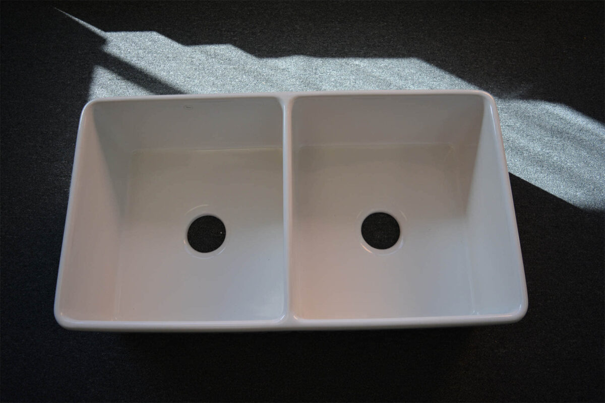 Double kitchen sink with sunlight on dark surface.