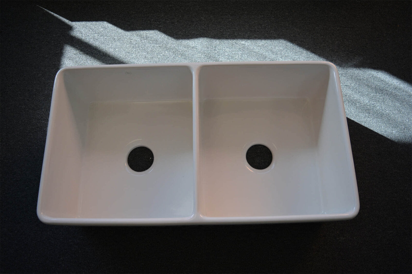 Double kitchen sink with sunlight on dark surface.