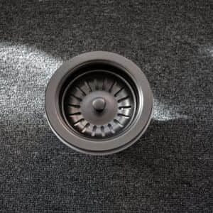 A stainless steel sink strainer on a dark carpet.