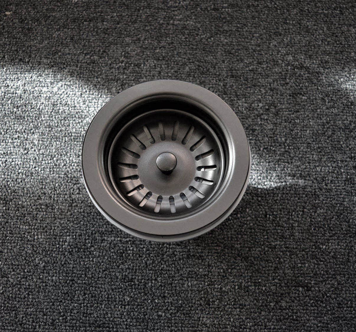 A stainless steel sink strainer on a dark carpet.