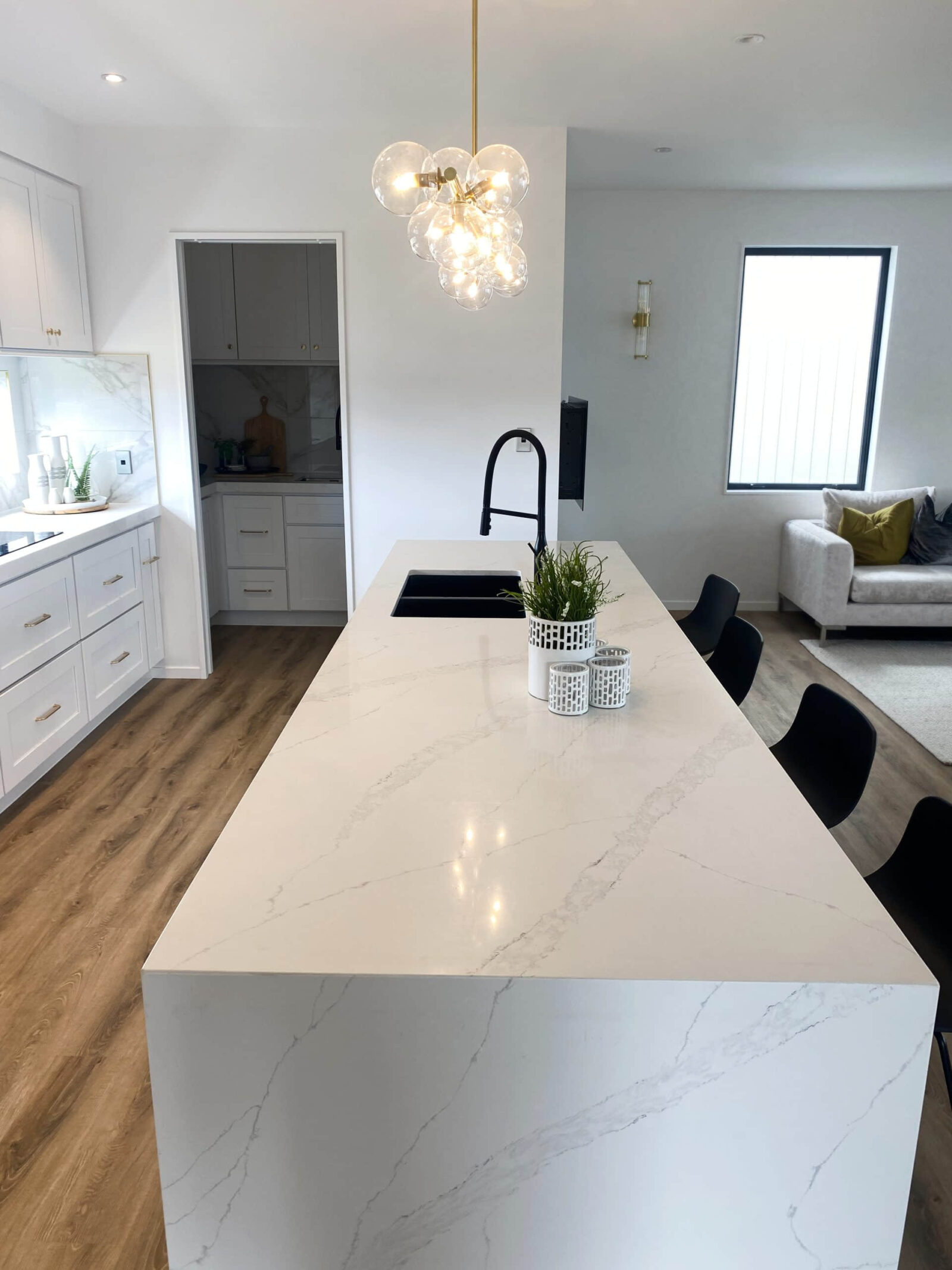 Modern kitchen with marble island, pendant light, and black chairs.