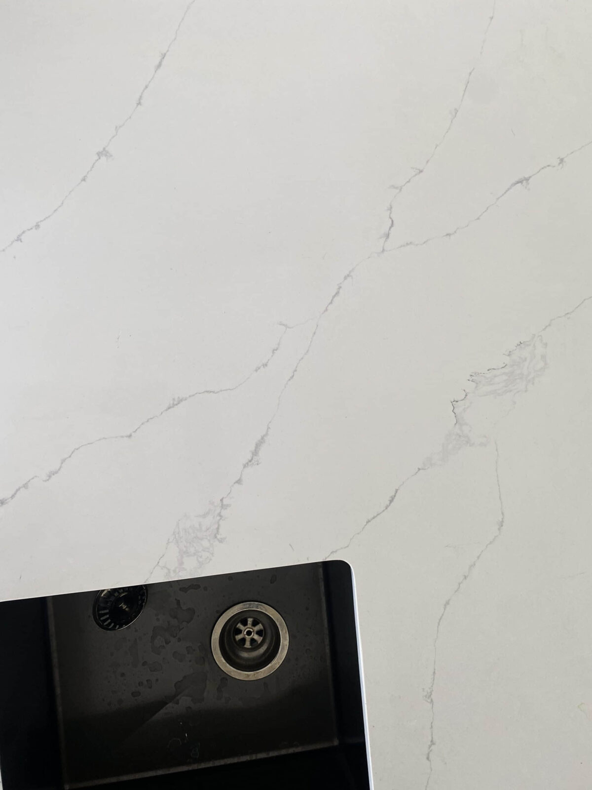 White marble countertop with subtle gray veining and a black sink corner.