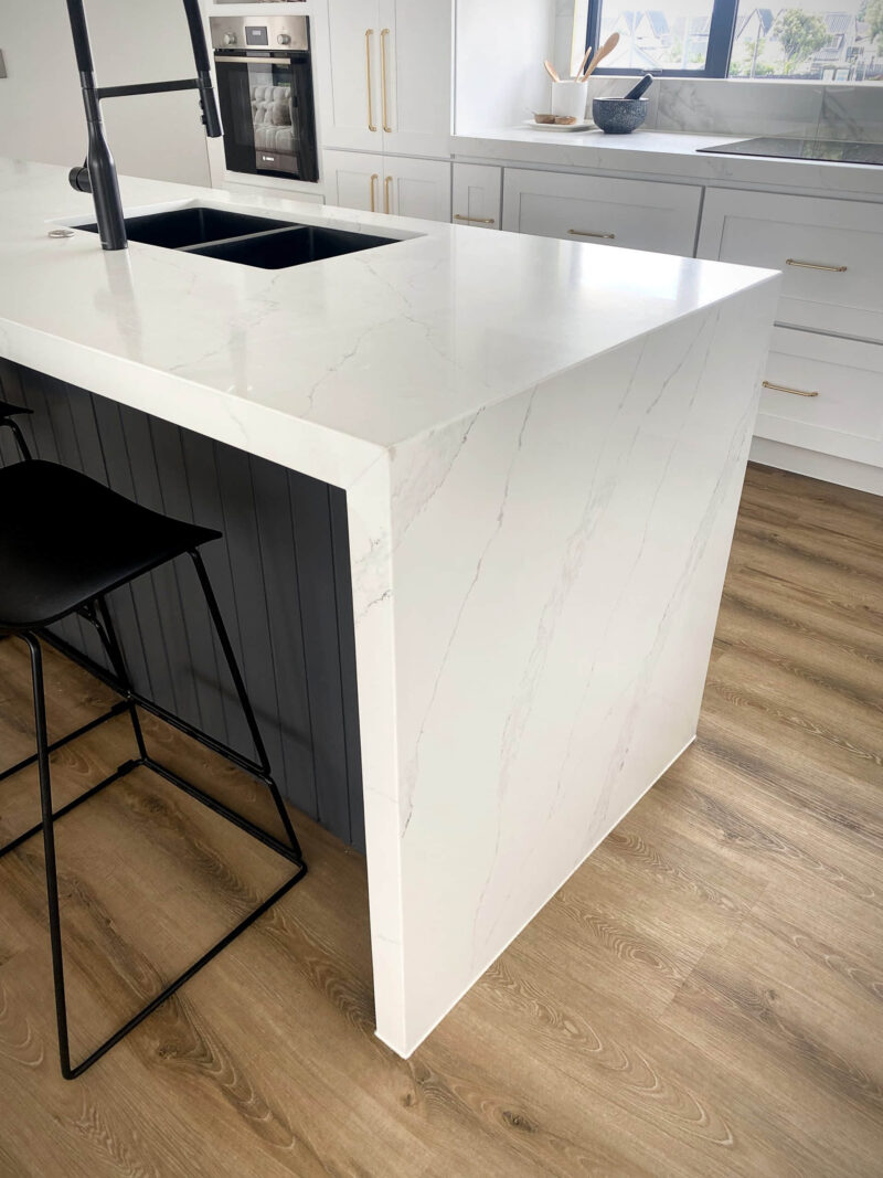 Modern kitchen with white marble countertop and black stool.