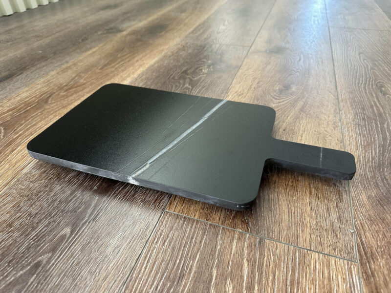 Black cutting board on wooden floor.