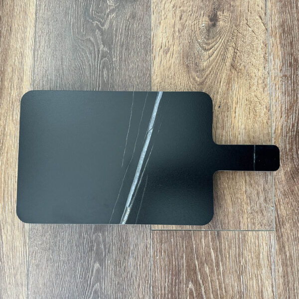 Black marble cutting board on wooden floor.