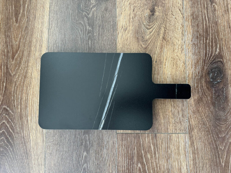 Black marble cutting board on wooden floor.