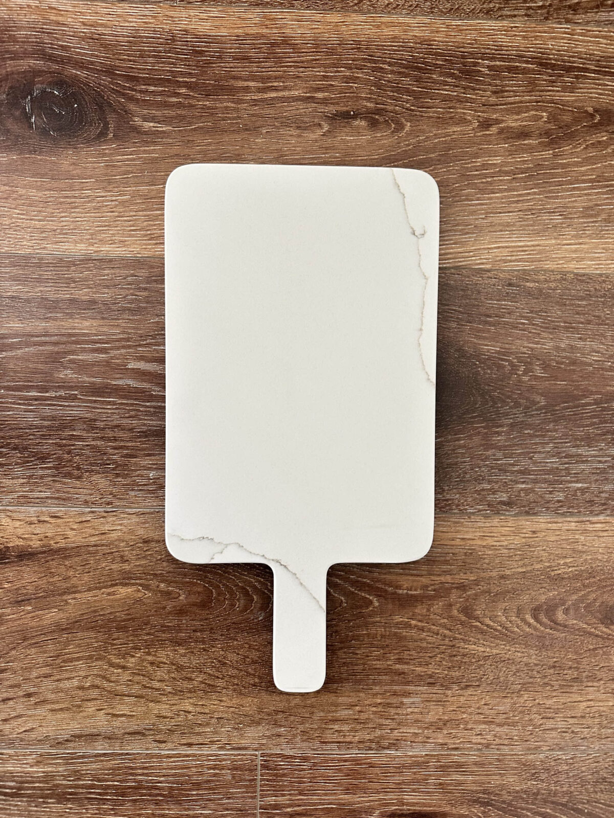 White marble cutting board on wooden surface.