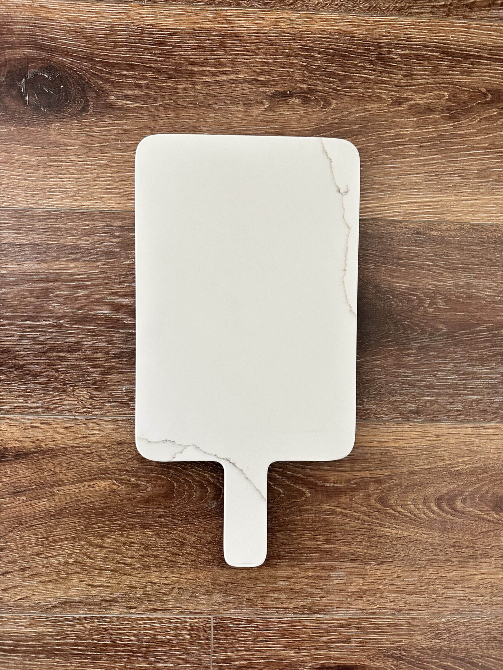 White marble cutting board on wooden surface.