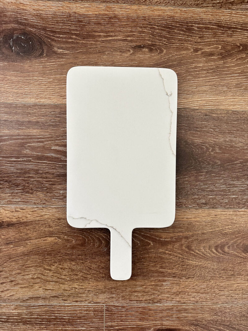 White marble cutting board on wooden surface.
