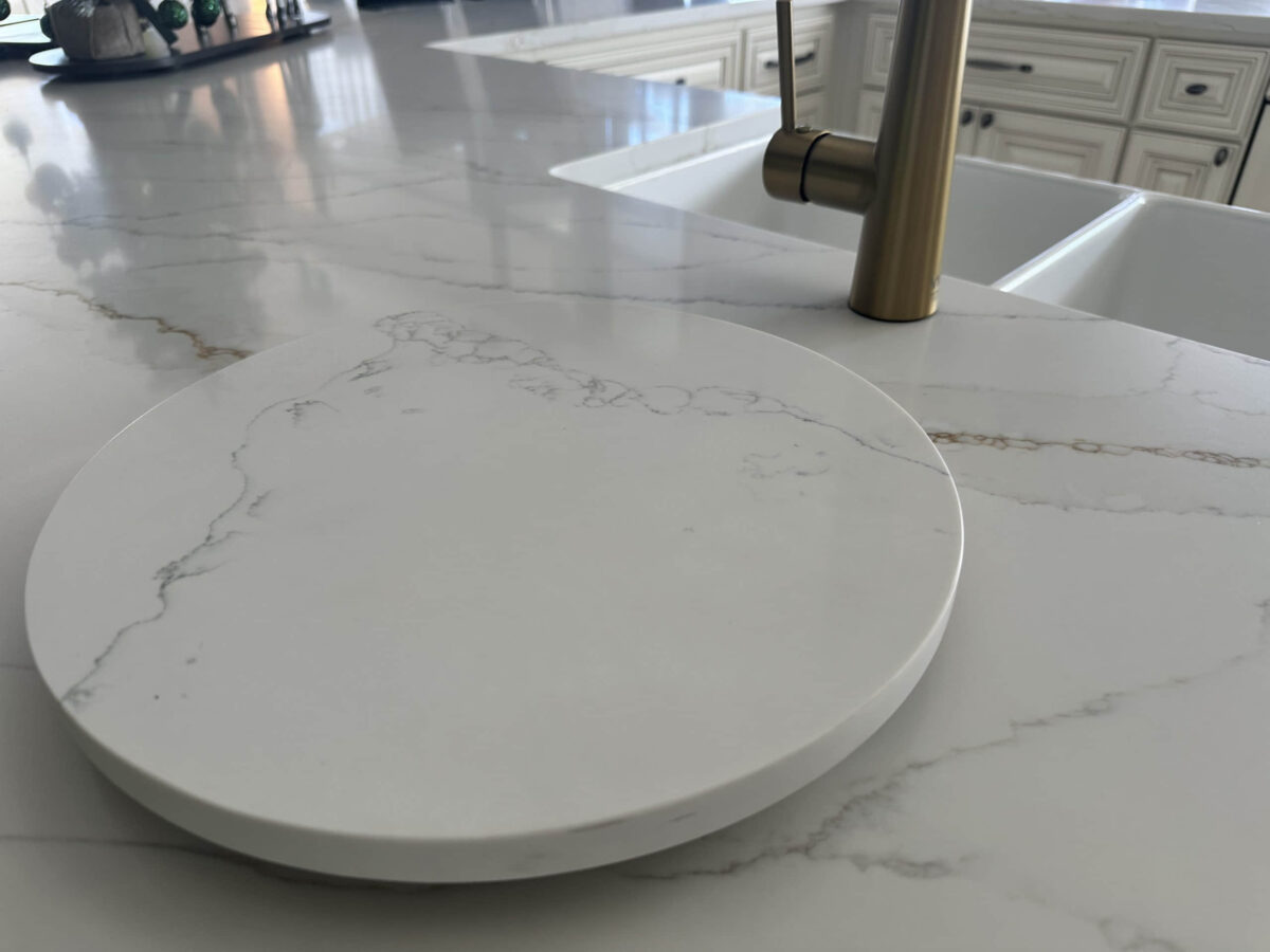 Marble kitchen countertop with round cutting board and gold faucet.