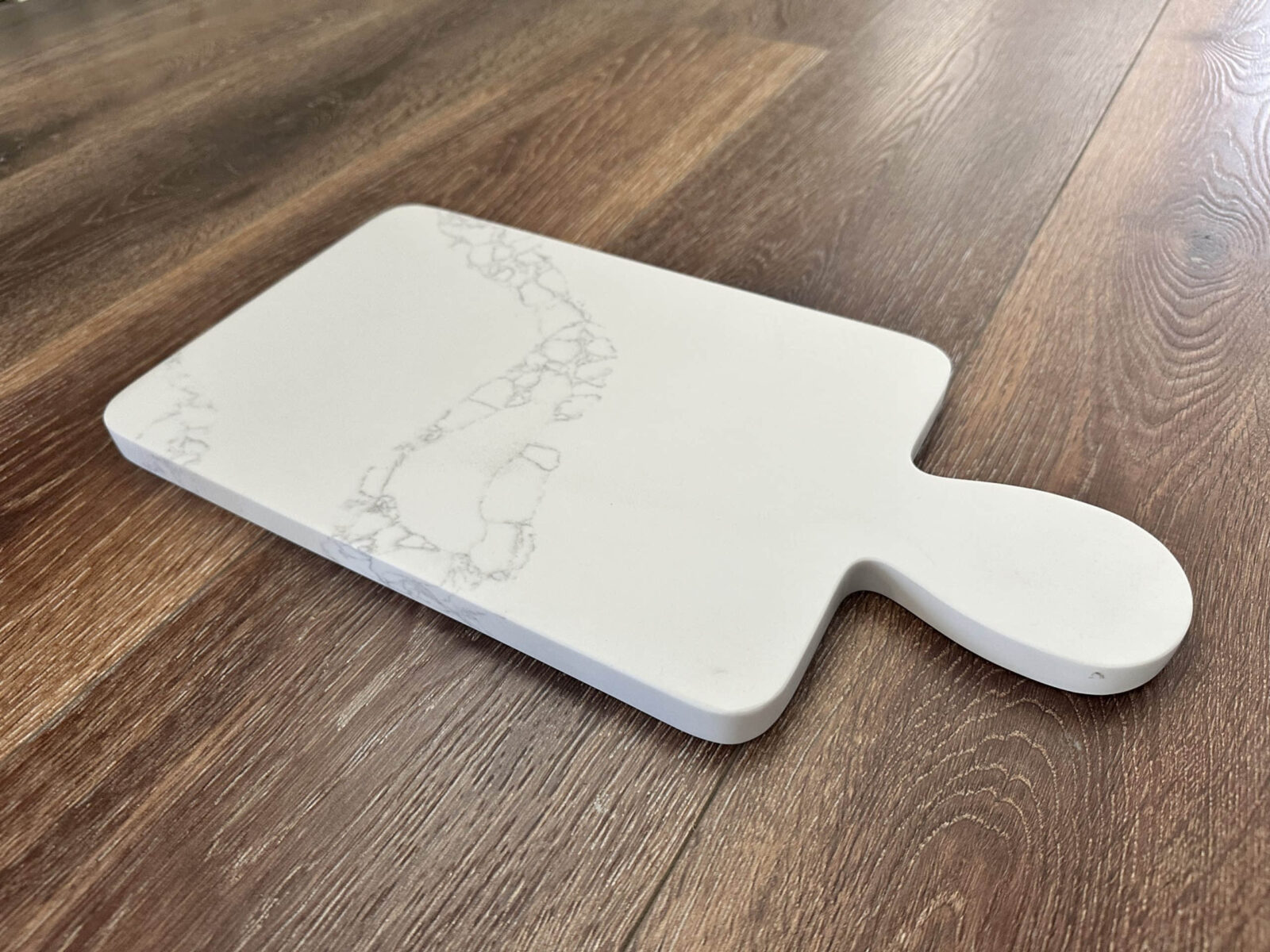 White marble cutting board on wooden floor.