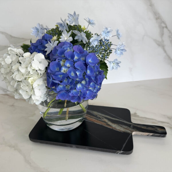 Blue and white hydrangeas in a glass vase on a marble countertop.
