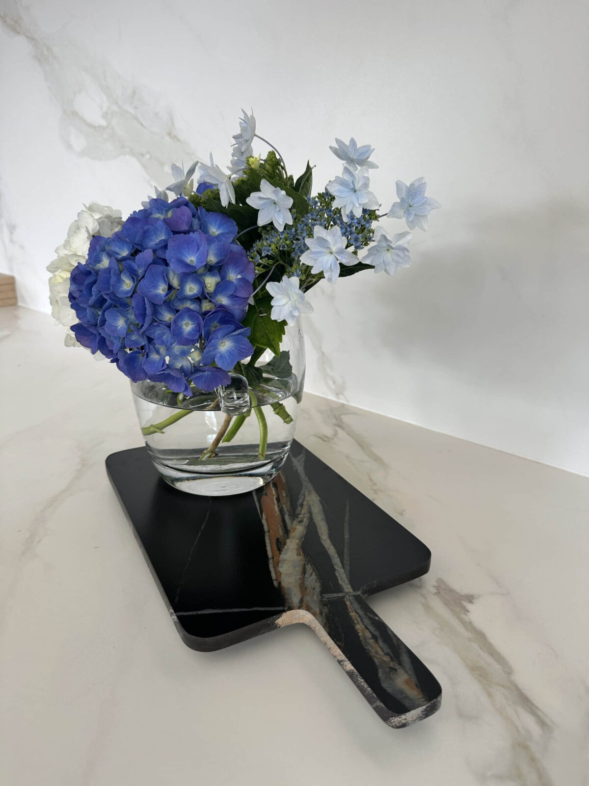 Blue and white flowers in a glass vase on a marble surface.