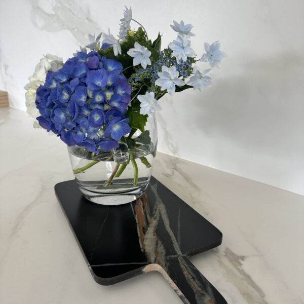 Blue and white flowers in a glass vase on a marble surface.