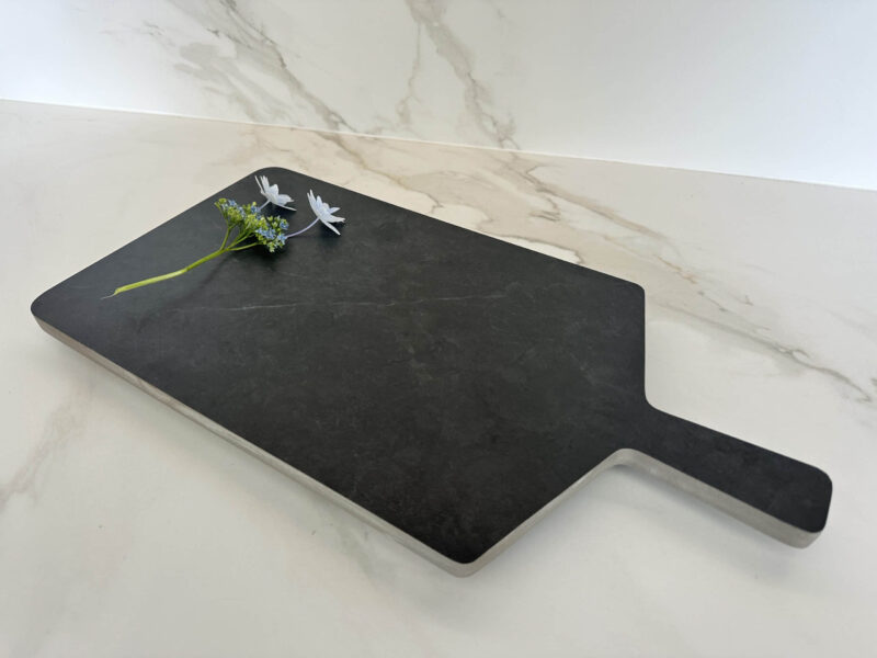 Black cutting board with flowers on marble countertop.