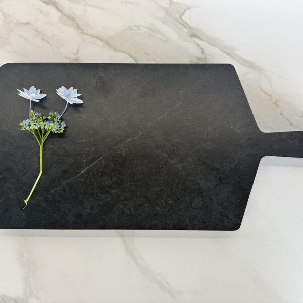 Black cutting board with two white flowers on a marble surface.