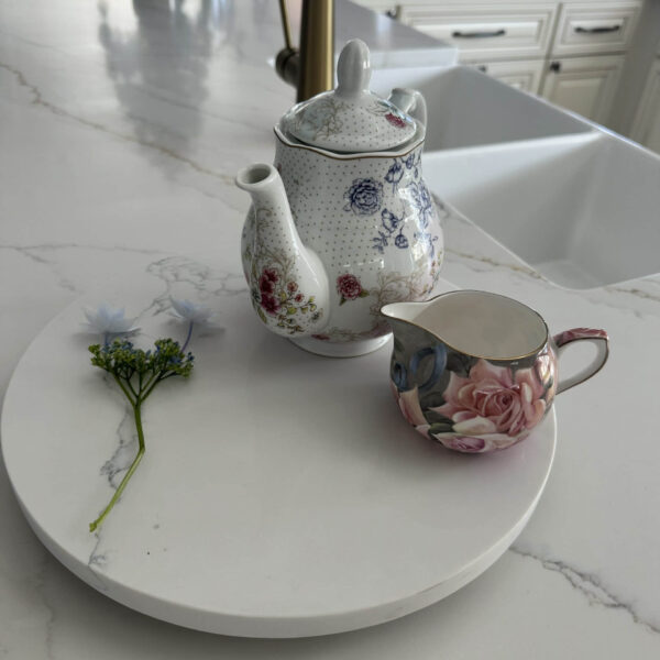 Floral teapot and creamer on marble counter with small flower.