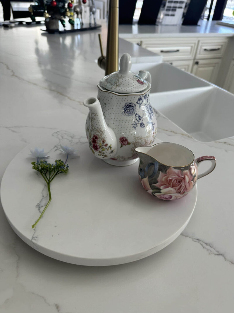 Floral teapot and creamer on marble counter with small flower.