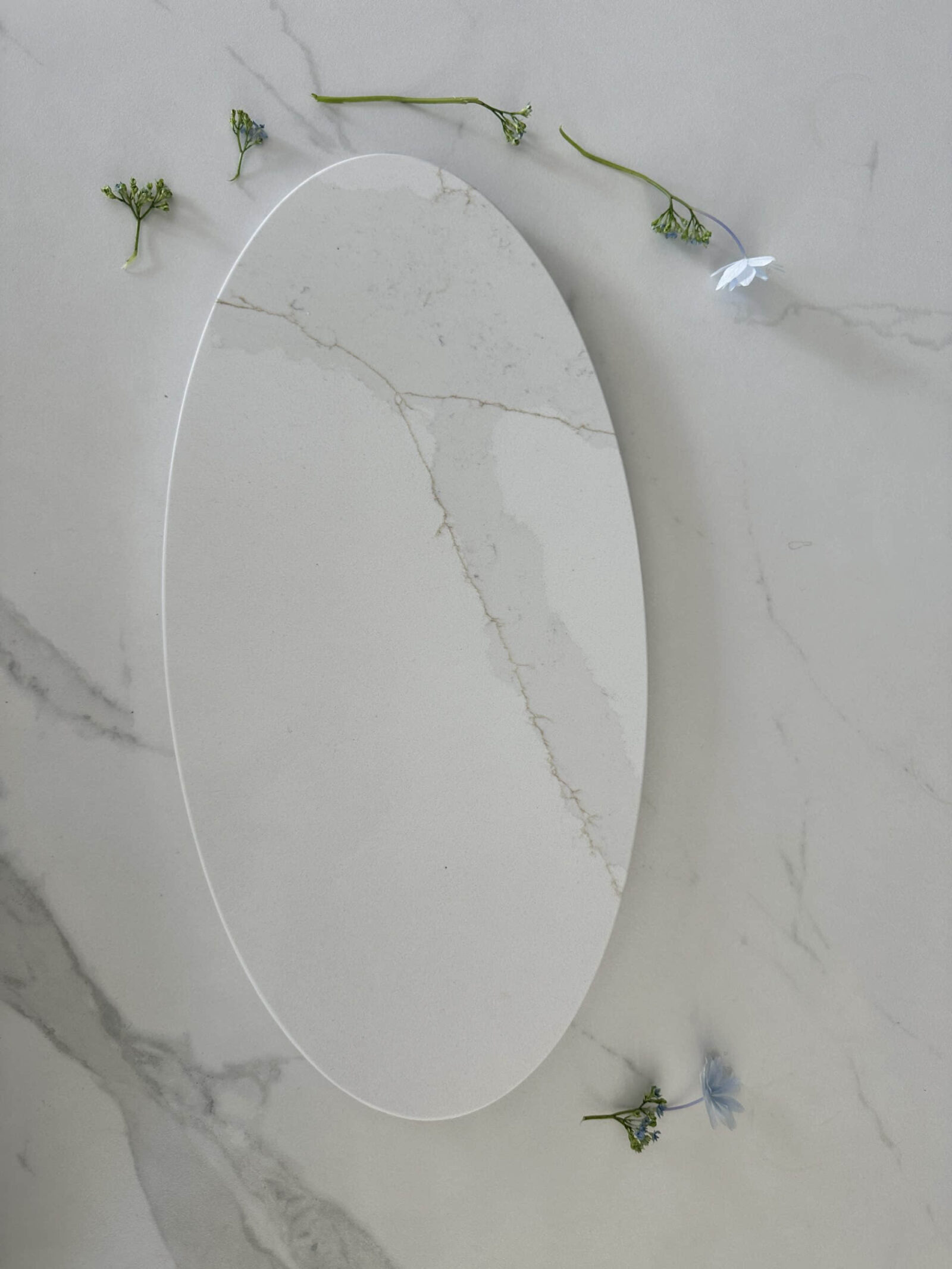 Oval marble platter on marble surface with scattered small flowers.
