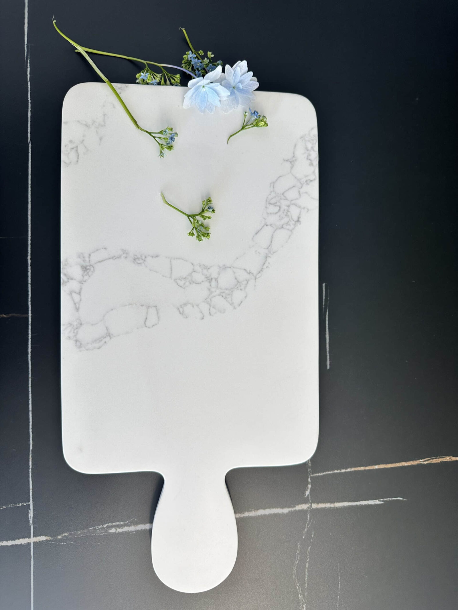 Marble cutting board with blue flowers on a dark surface.