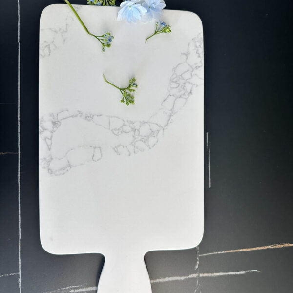 Marble cutting board with blue flowers on a dark surface.