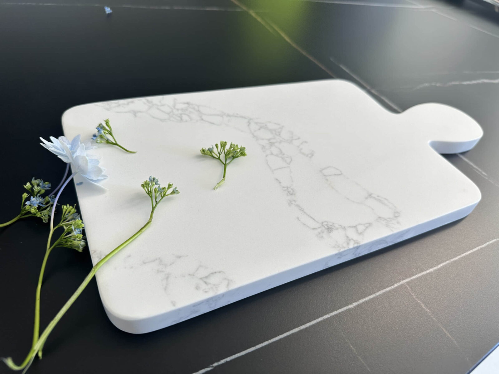 Marble cutting board with small flowers on a dark surface.