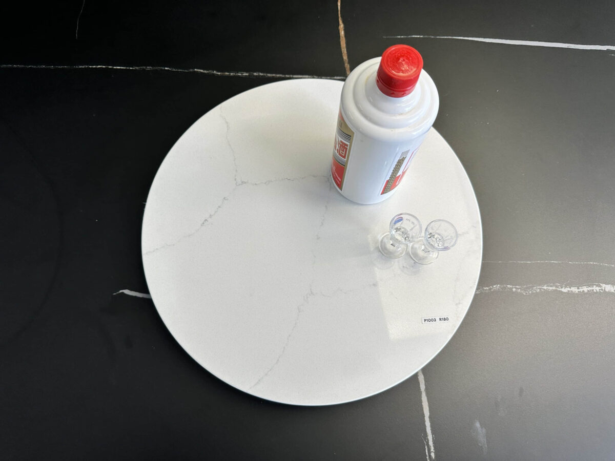 Marble lazy Susan with a bottle and small cups on a black surface.