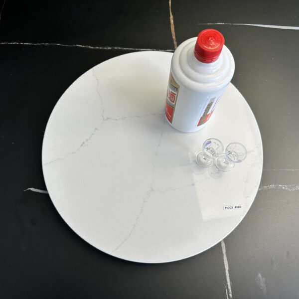 Marble lazy Susan with a bottle and small cups on a black surface.