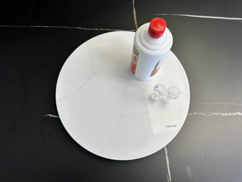 Marble lazy Susan with a bottle and small cups on a black surface.