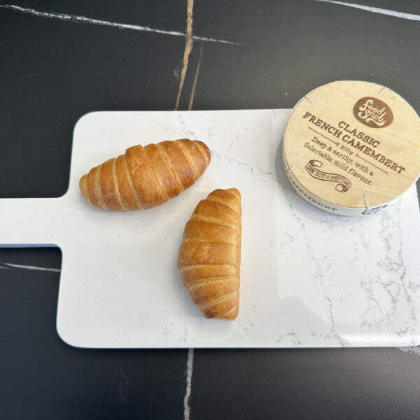 Two croissants and camembert on a white cutting board.