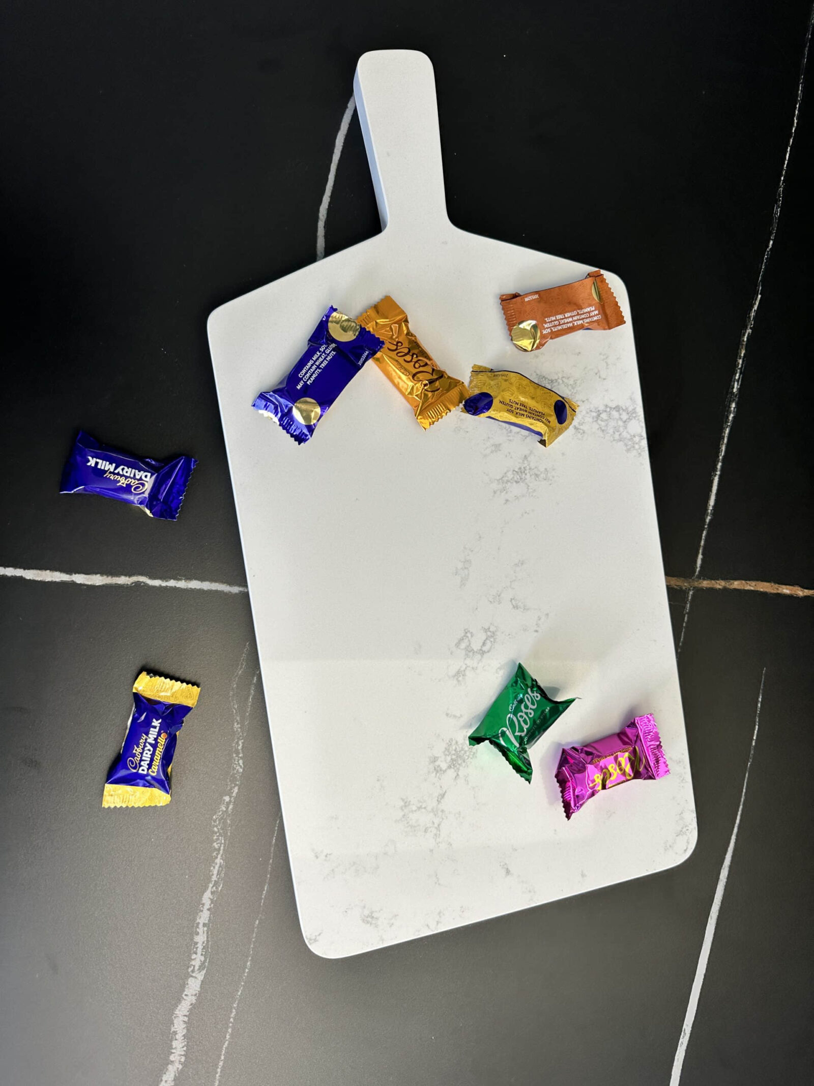 Marble cutting board with assorted wrapped chocolates on a dark surface.