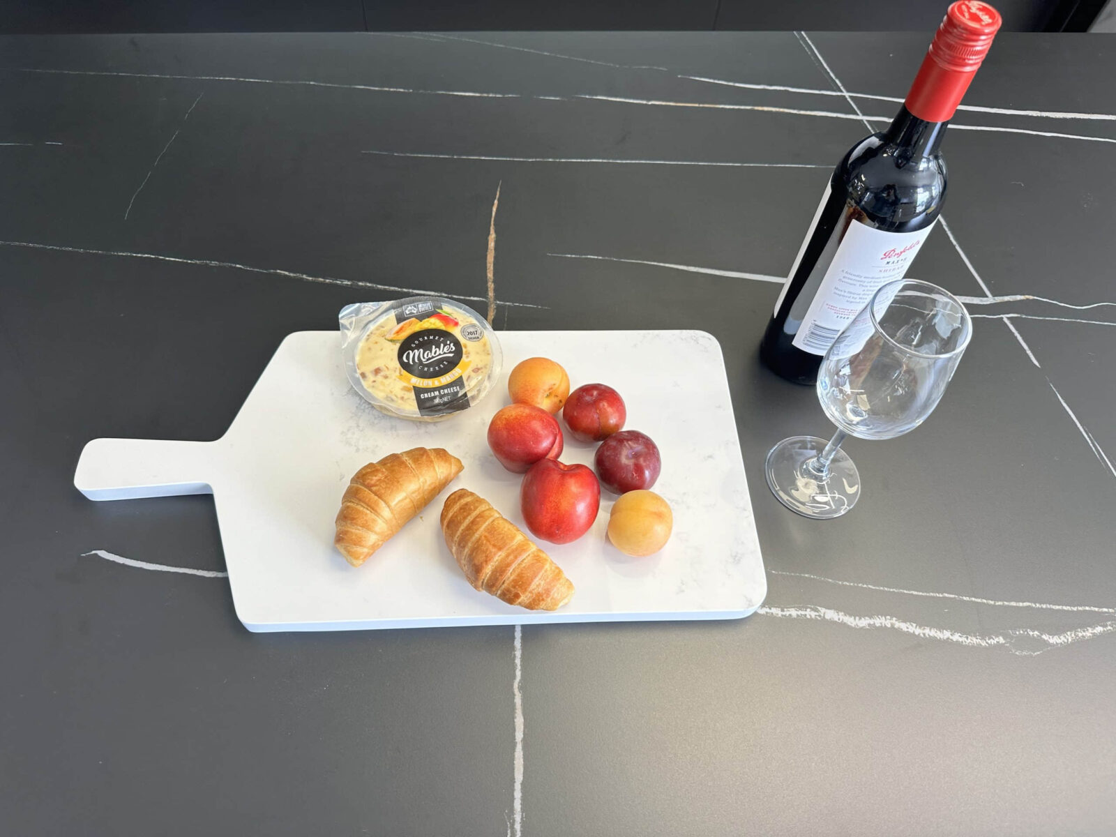 Cheese, croissants, plums, and wine on a marble cutting board.