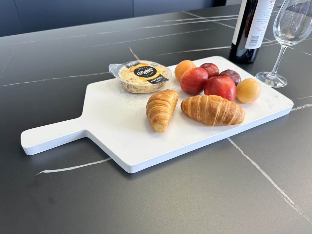 Cheese, croissants, and fruit on a cutting board with wine and glass nearby.