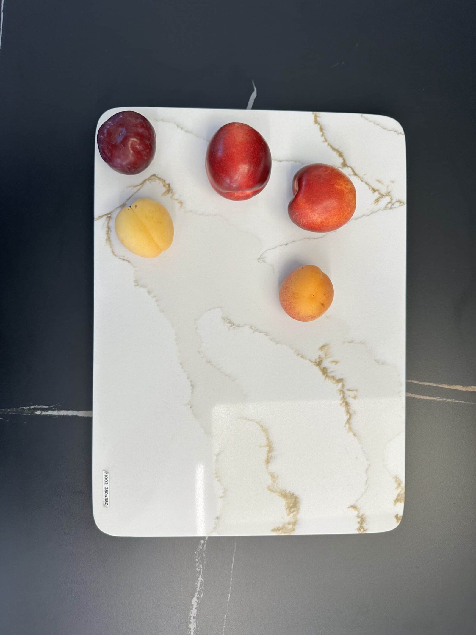 Five fruits on a marble cutting board.