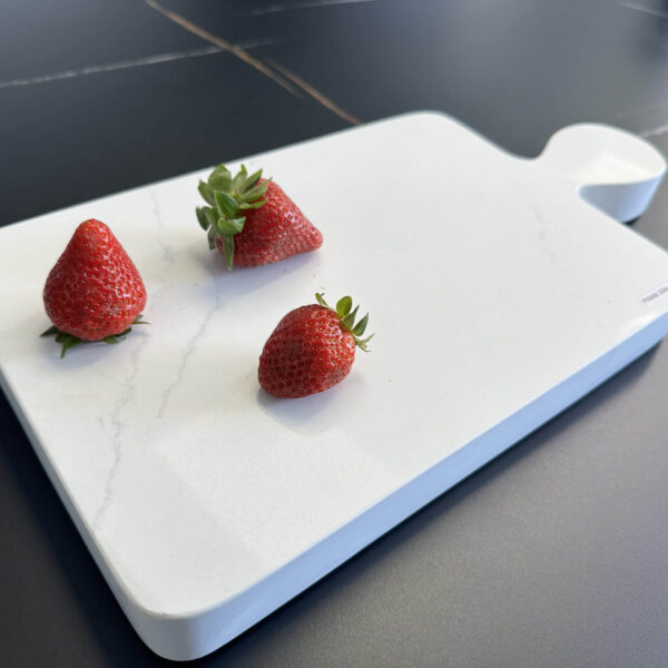 Three strawberries on a white cutting board.