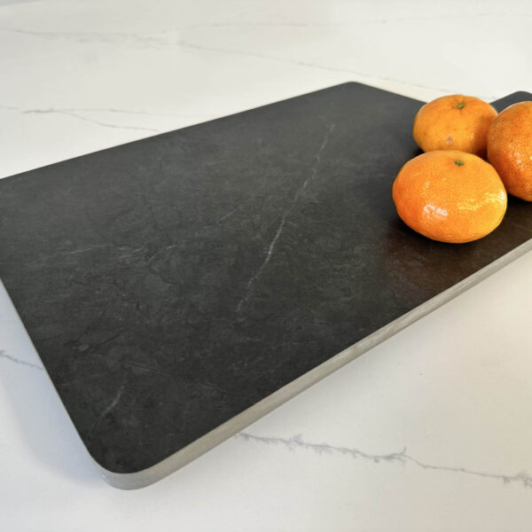Cutting board with three oranges on a marble countertop.
