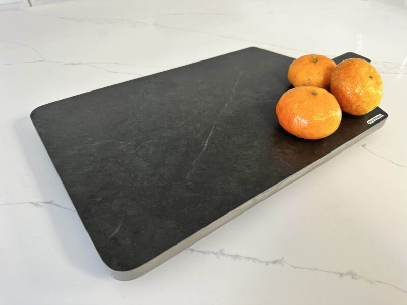 Cutting board with three oranges on a marble countertop.