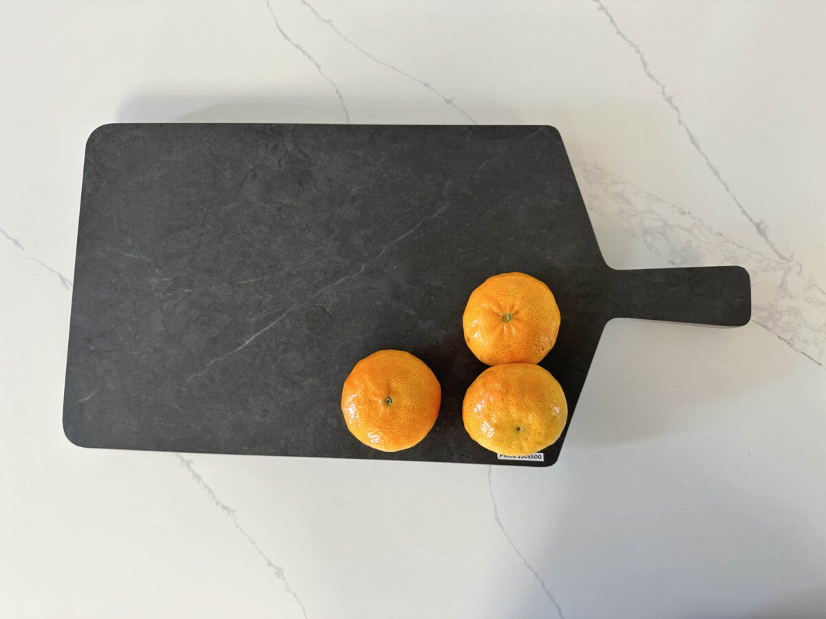 Three oranges on a black cutting board on a marble countertop.