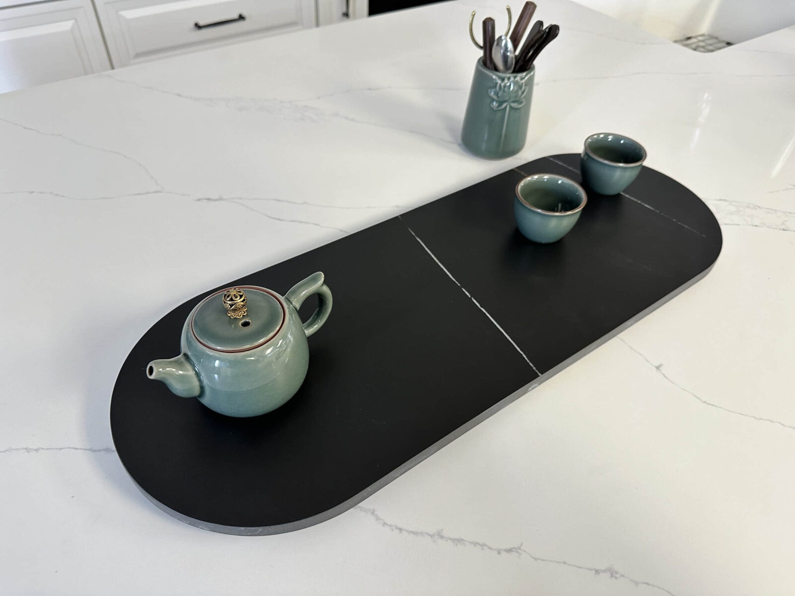 Ceramic teapot and cups on a black serving tray in a kitchen.