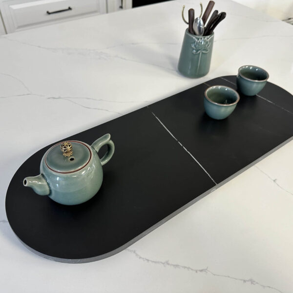 Ceramic teapot and cups on a black serving tray in a kitchen.