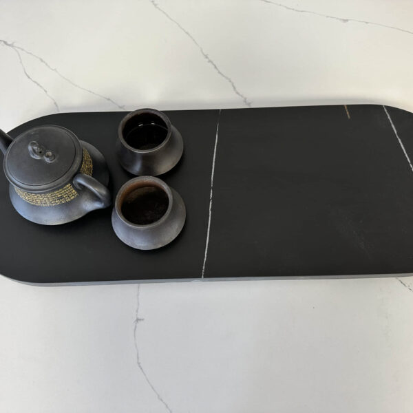 Black teapot and cups on a dark serving tray.