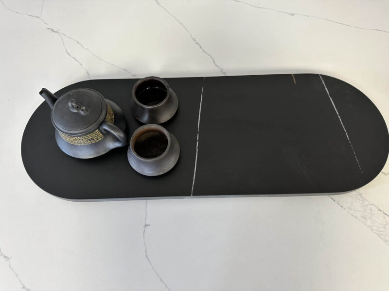 Black teapot and cups on a dark serving tray.