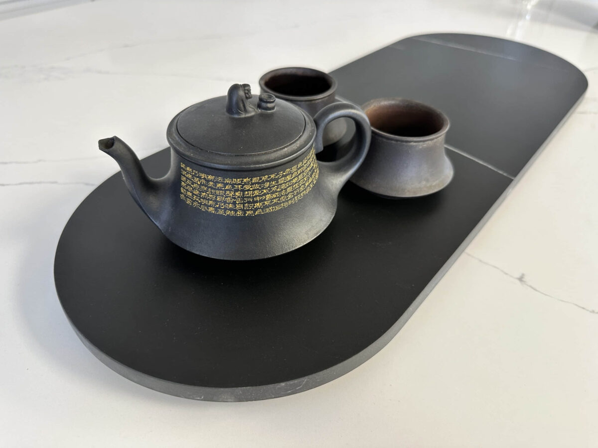 Black teapot and cups on a sleek black tray.