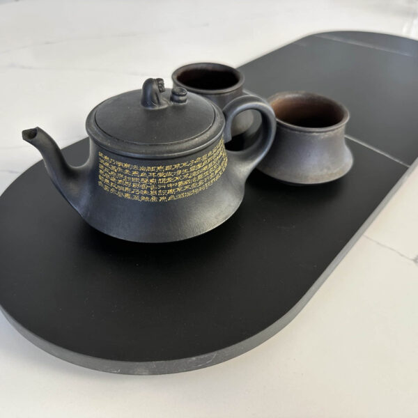 Black teapot and cups on a sleek black tray.