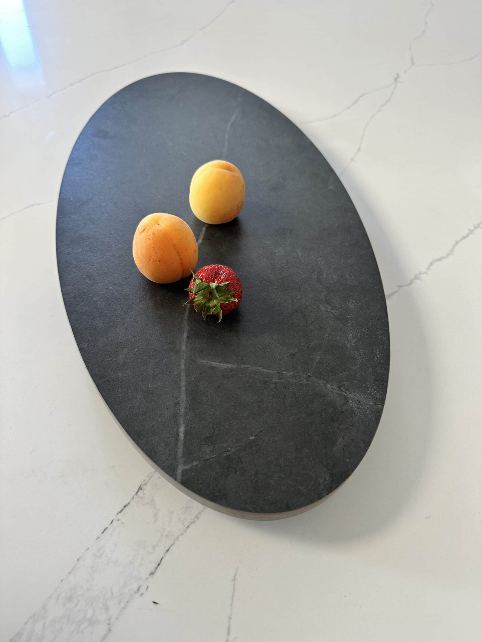 Two apricots and a strawberry on a dark oval platter.