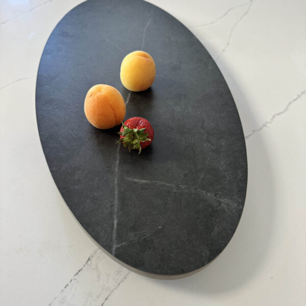 Two apricots and a strawberry on a dark oval platter.