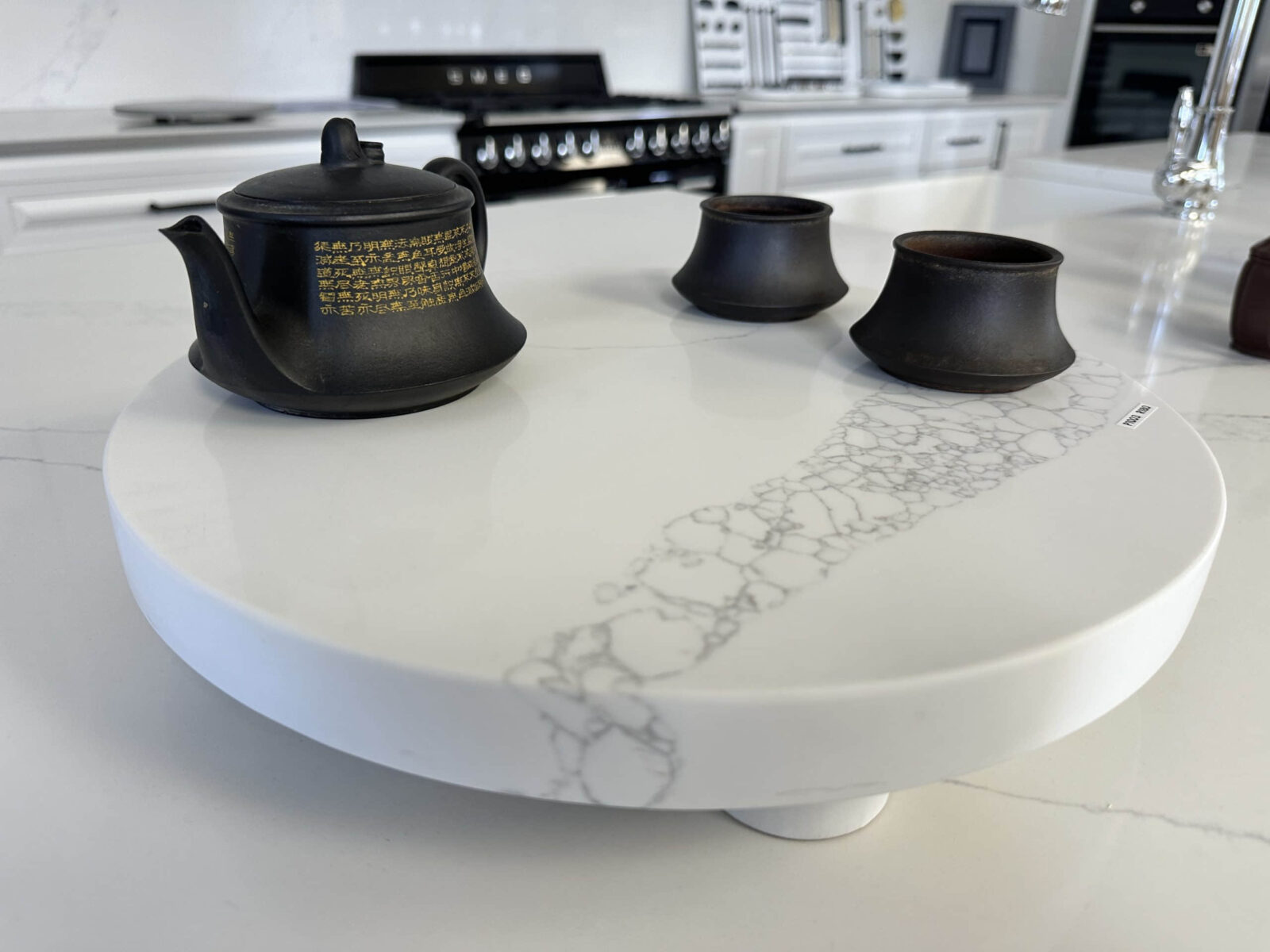 Black teapot and cups on a white marble kitchen counter.